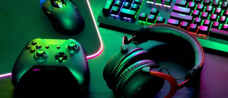 Herní ovladač vedle klávesnice myš a klávesnice svítí zelenými a fialovými světly