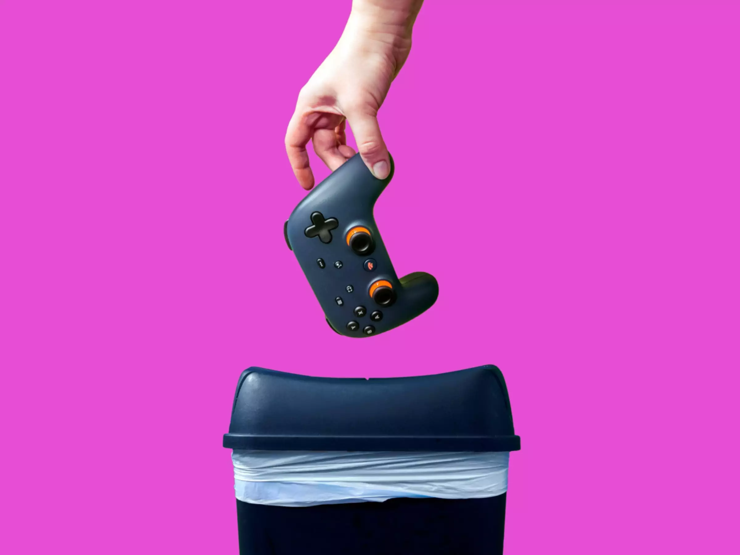 在粉红色背景下，谷歌Stadia游戏控制器被扔进垃圾桶的特写。