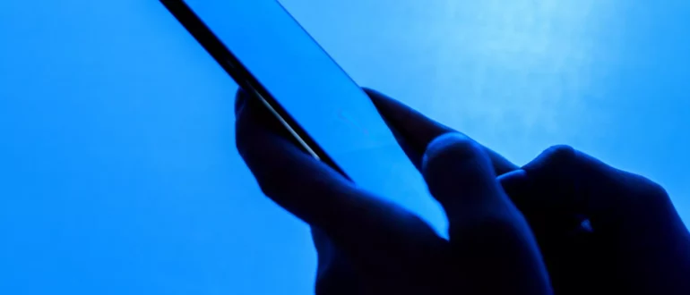 Bližnji posnetek rok, ki držijo telefon, na modrem ozadju