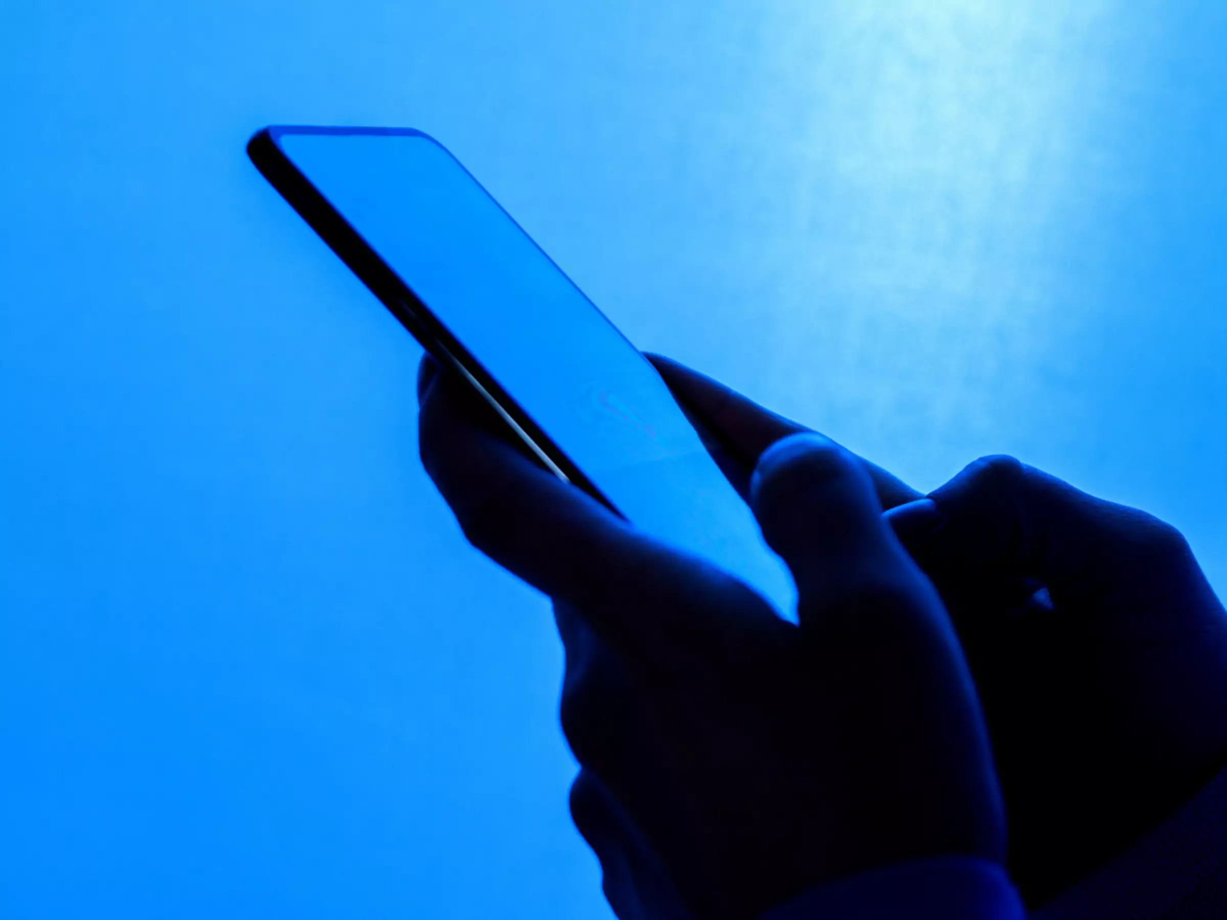 Bližnji posnetek rok, ki držijo telefon, na modrem ozadju