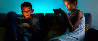 Dvě malé děti sedí na gauči a hrají hry na chytrých telefonech