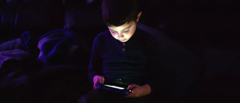 Jeune enfant jouant sur une tablette dans une pièce sombre