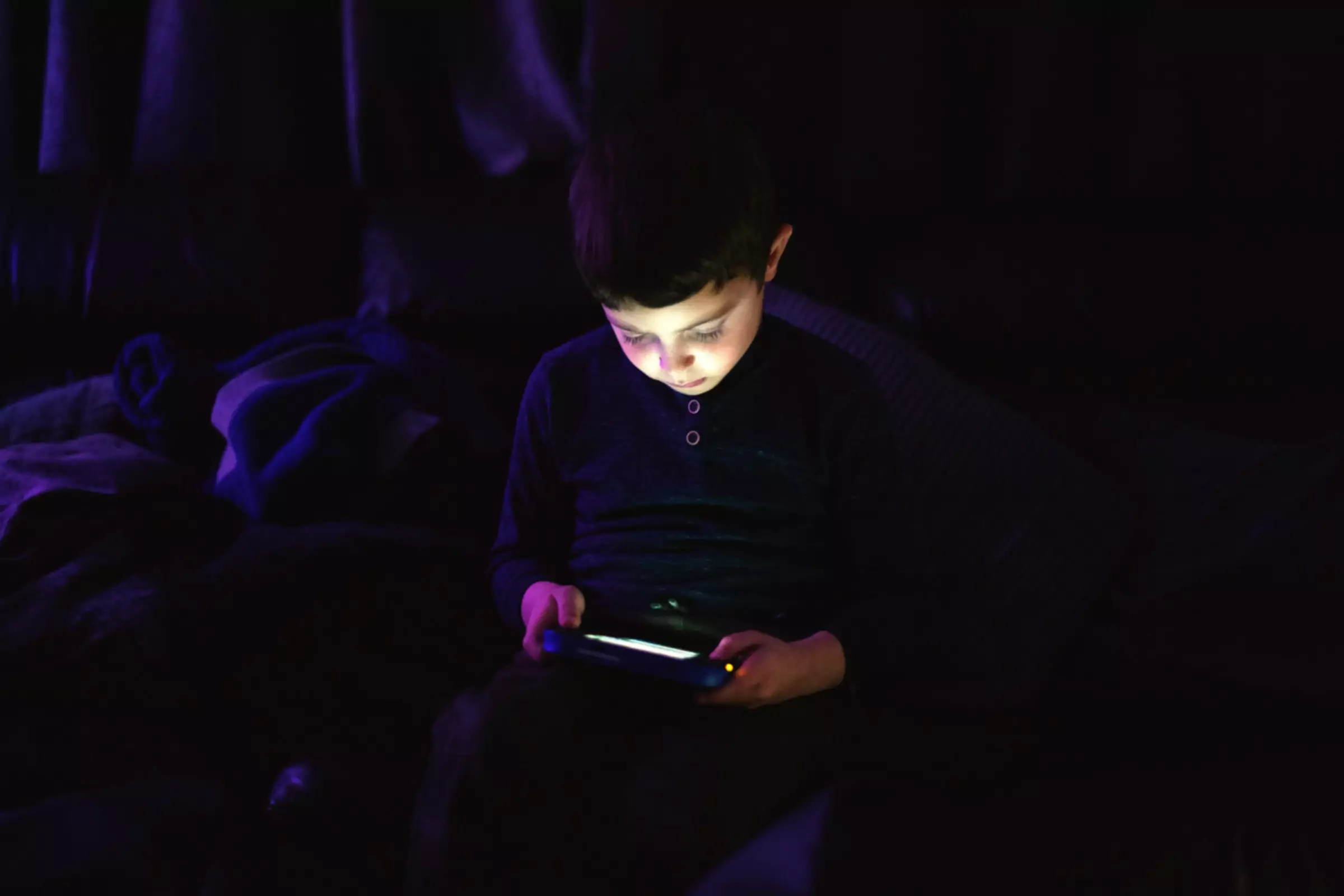 copil mic joc pe tabletă în cameră întunecată